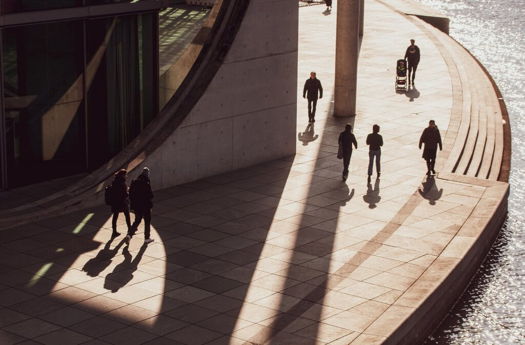 People near an aesthetic building are walking in the sun and shade and being shot from above
