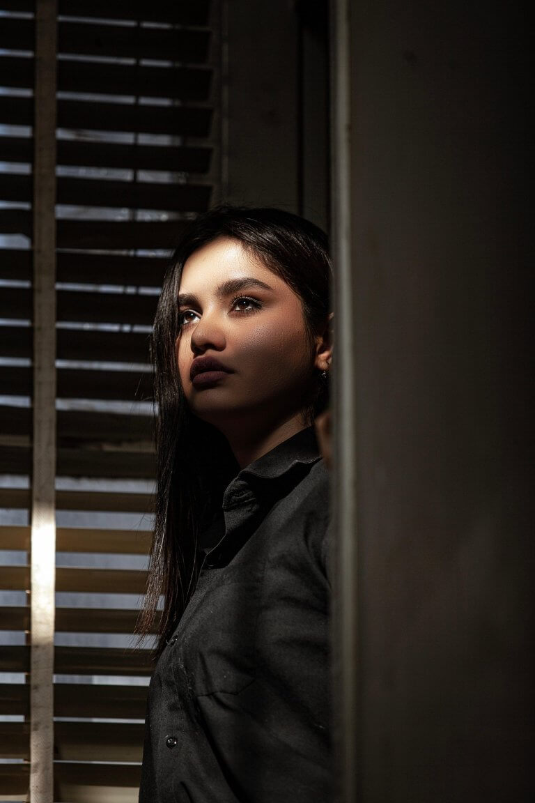 Woman is standing at the window lost in thought and the sun is shining in her face
