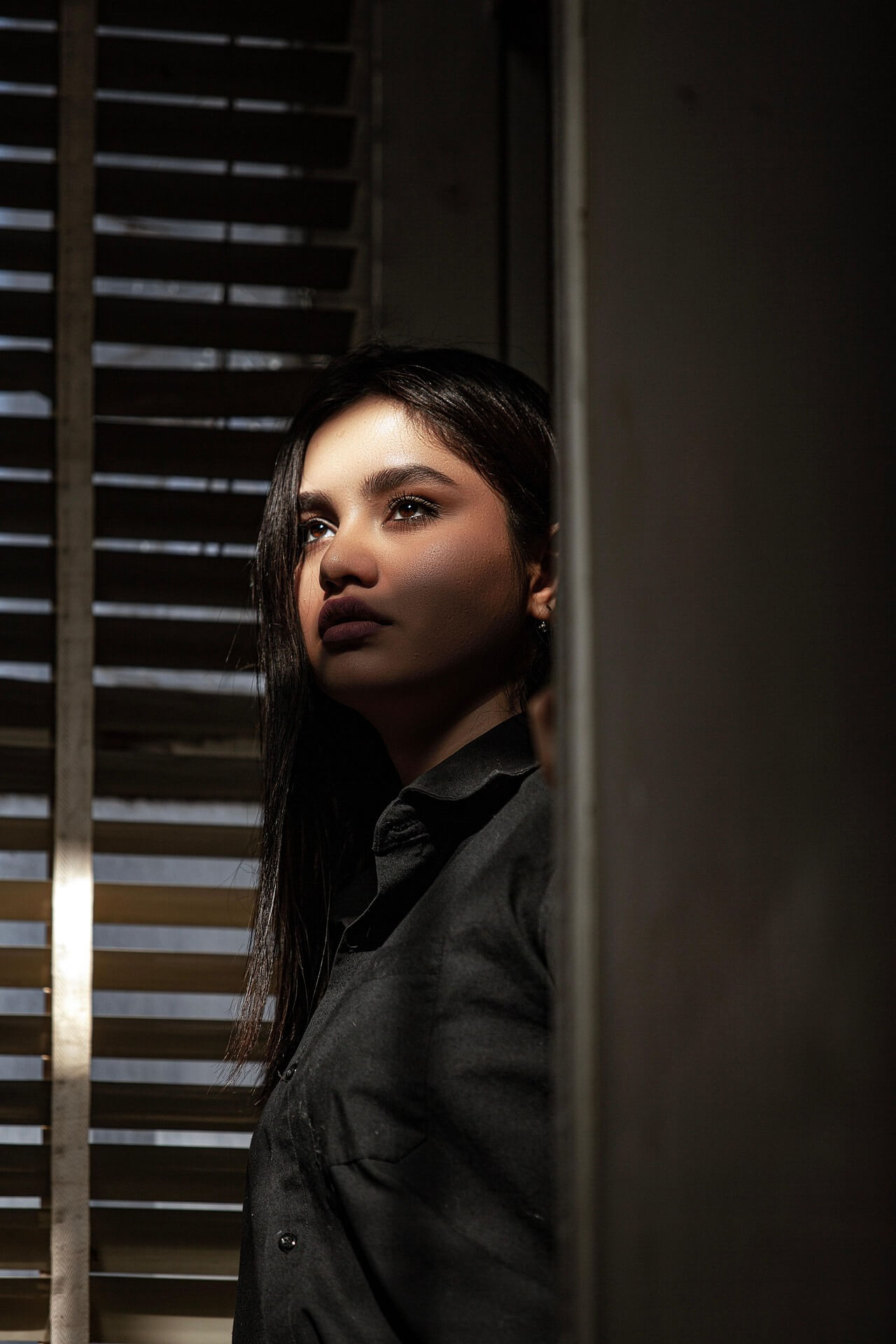 Woman is standing at the window lost in thought and the sun is shining in her face