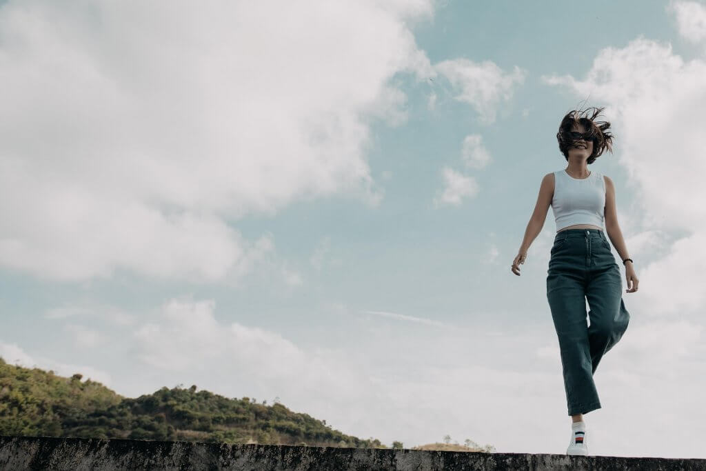 Woman is dancing on a hill and is being shot from below with the sky filling the picture