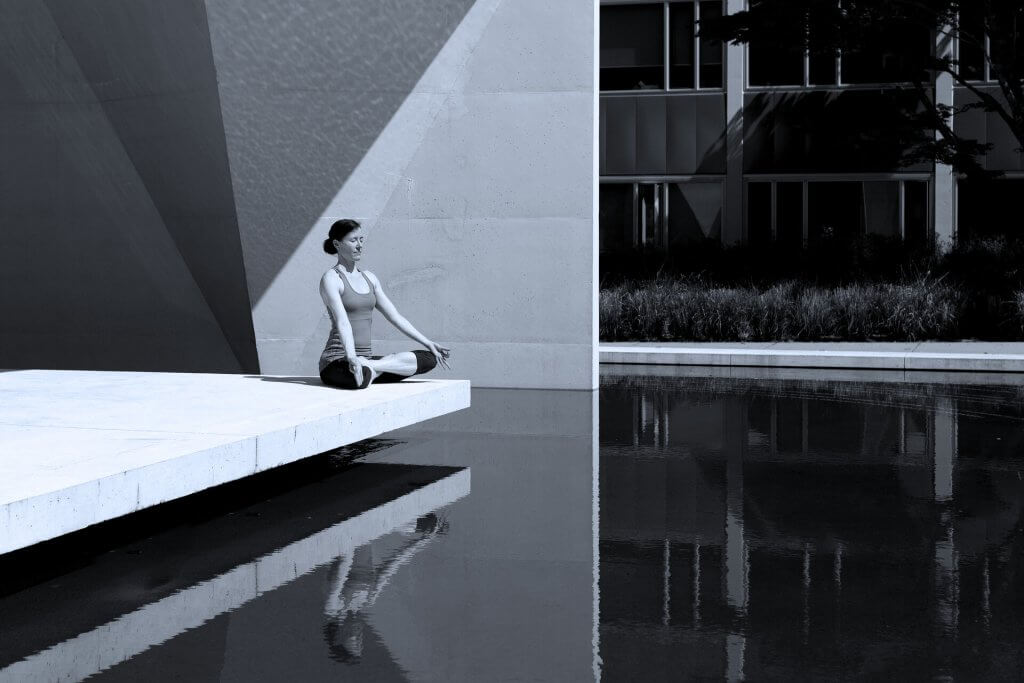Woman sits on a platform near water and meditates in a yoga position