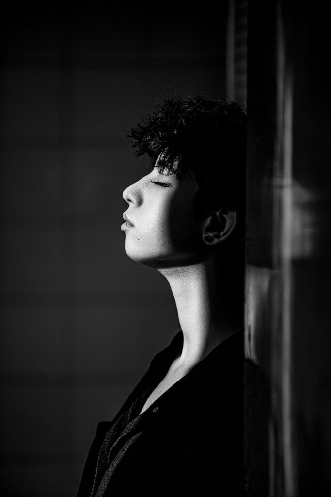 Woman is leaning on a wall and thinking with the sun shining on her face in black and white